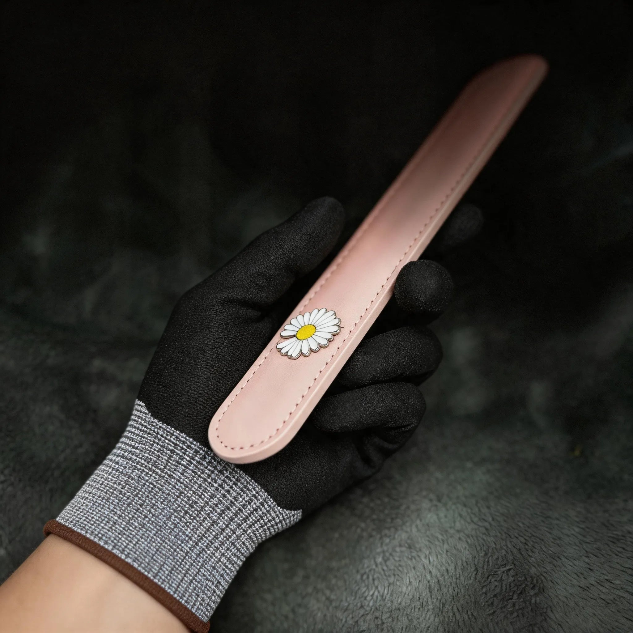 Daisy Hush Slim Leather Spanking Paddle angled on black satin, showing blush pink leather and daisy accent.