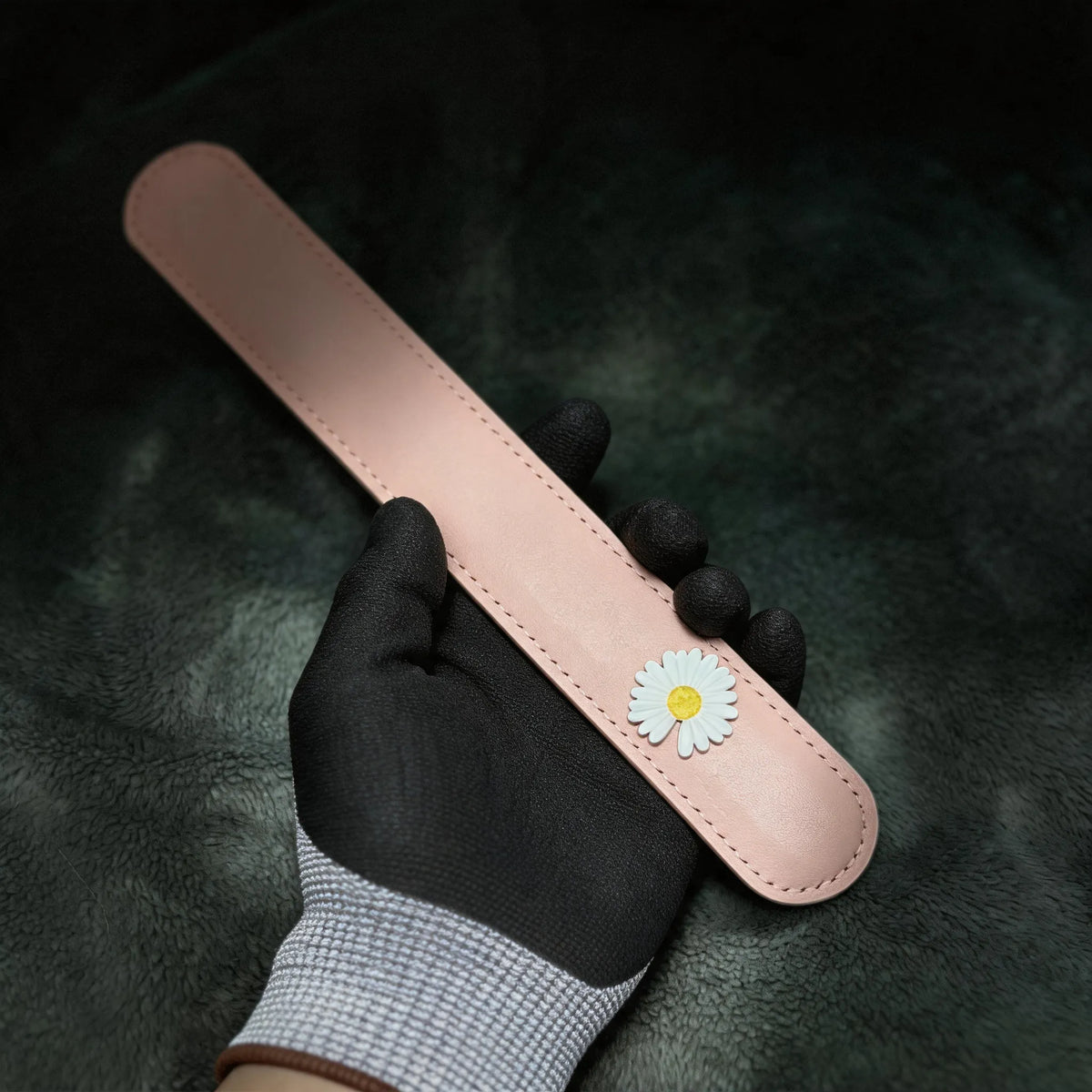 Daisy Hush Slim Leather Spanking Paddle hand-held studio detail showing daisy accent and stitched edge.