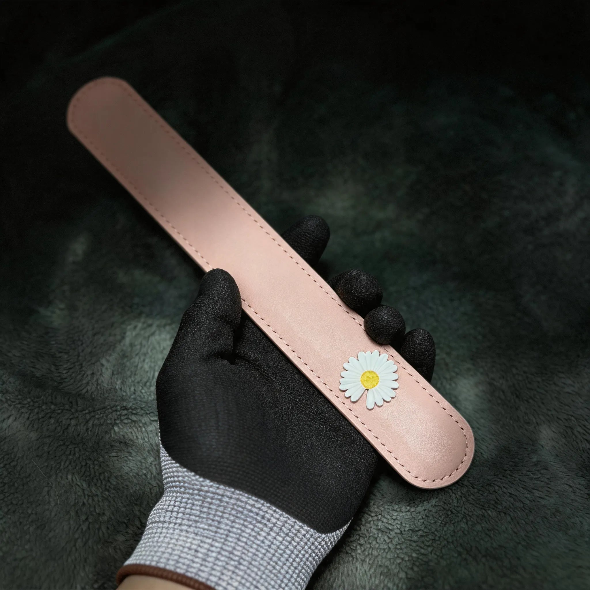 Daisy Hush Slim Leather Spanking Paddle hand-held studio detail showing daisy accent and stitched edge.