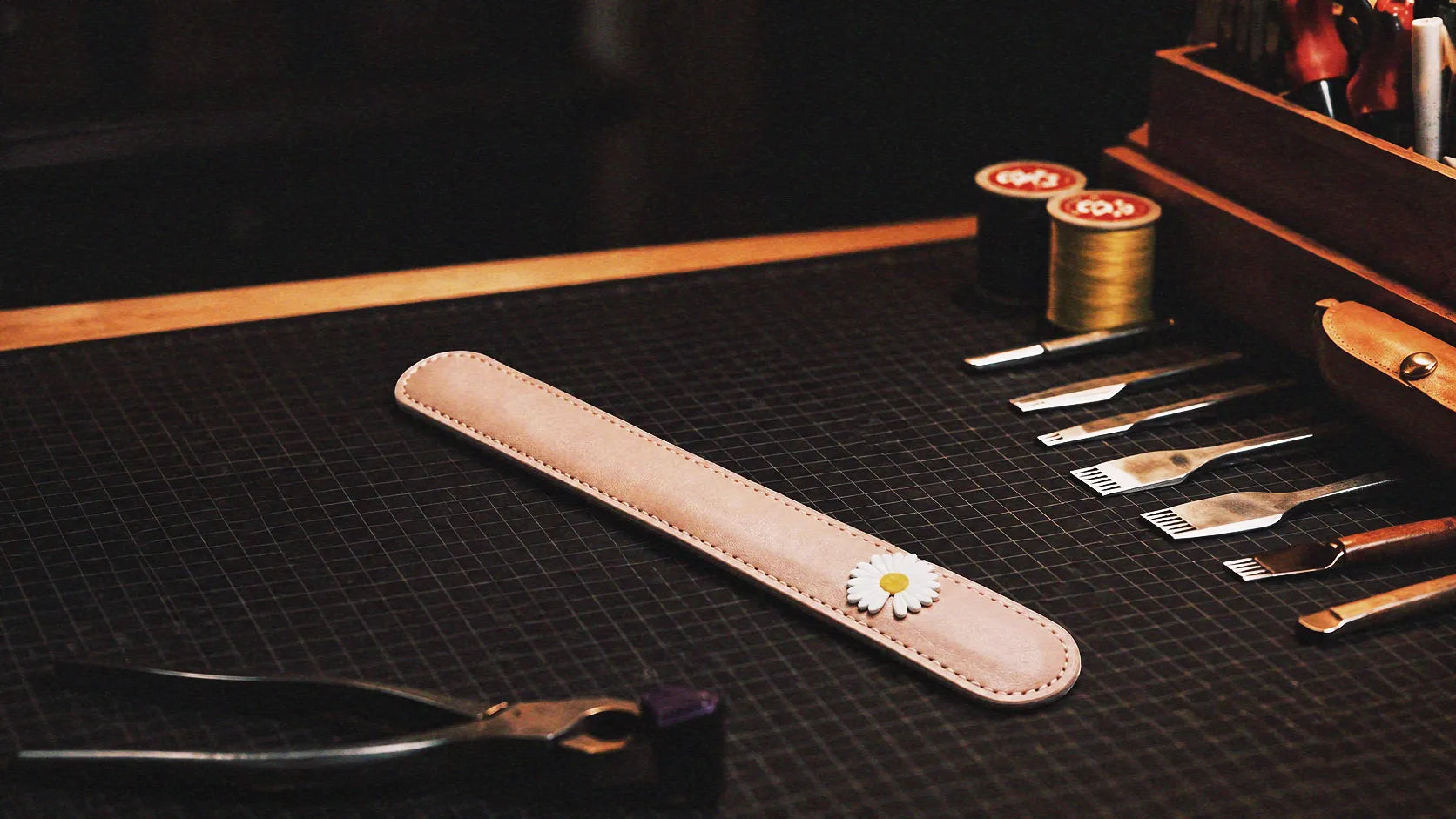 Daisy Hush Slim Leather Spanking Paddle warm tabletop studio scene with wooden box, blush pink leather, and daisy accent.