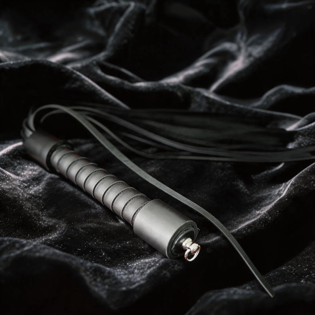 Midnight Discipline Leather Flogger angled on black satin, showing matte black leather and slim tails.