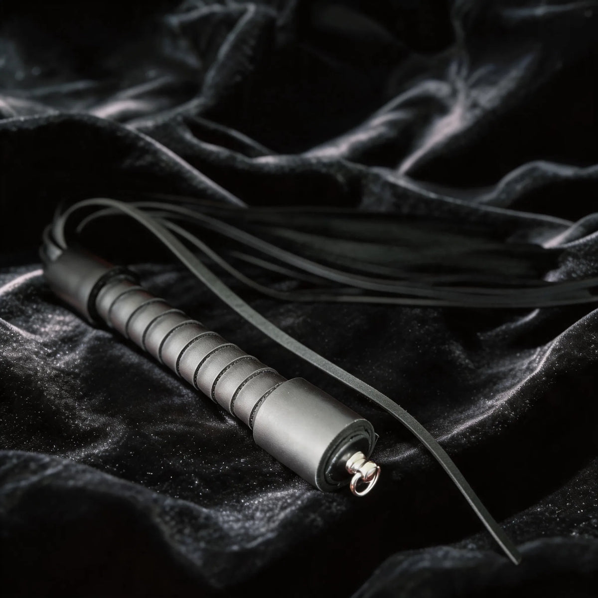 Midnight Discipline Leather Flogger angled on black satin, showing matte black leather and slim tails.