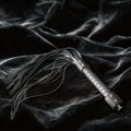 Midnight Discipline Leather Flogger matte black leather flogger on black satin with slim tails.