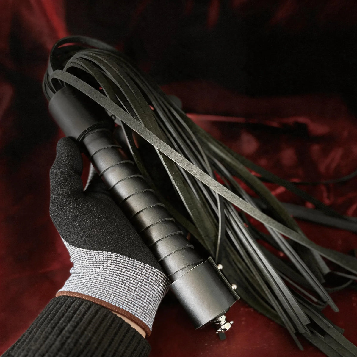 Midnight Discipline Leather Flogger hand-held studio detail showing slim tails and wrapped handle.
