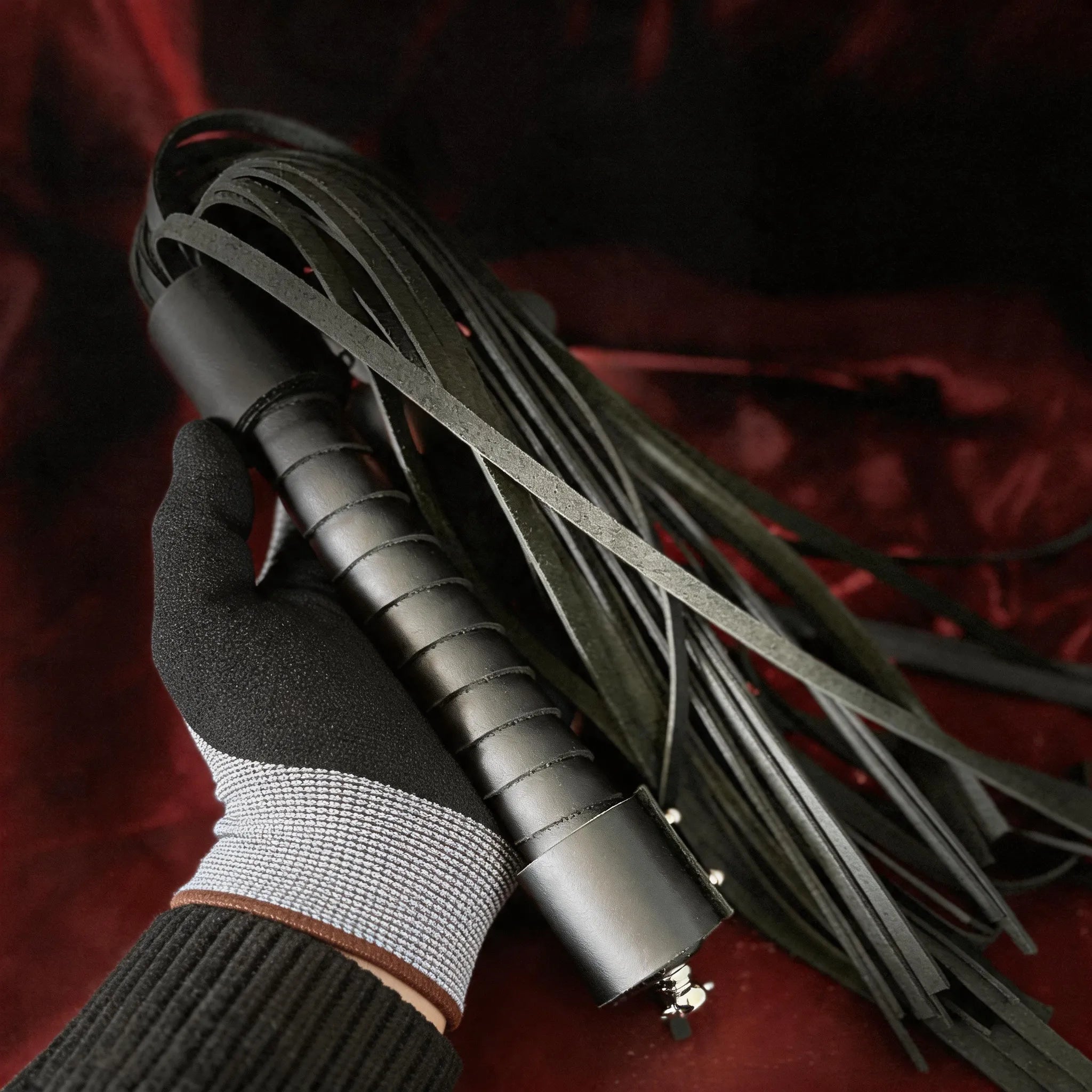 Midnight Discipline Leather Flogger hand-held studio detail showing slim tails and wrapped handle.