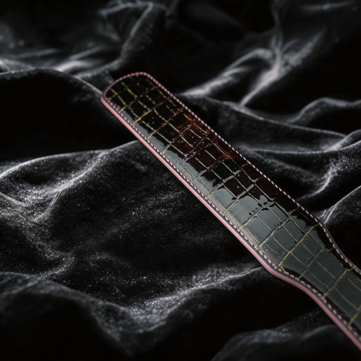 Noir Grid Patent Texture Leather Paddle hand-held studio detail showing grid texture and glossy edge.
