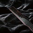 Noir Grid Patent Texture Leather Paddle hand-held studio detail showing grid texture and glossy edge.