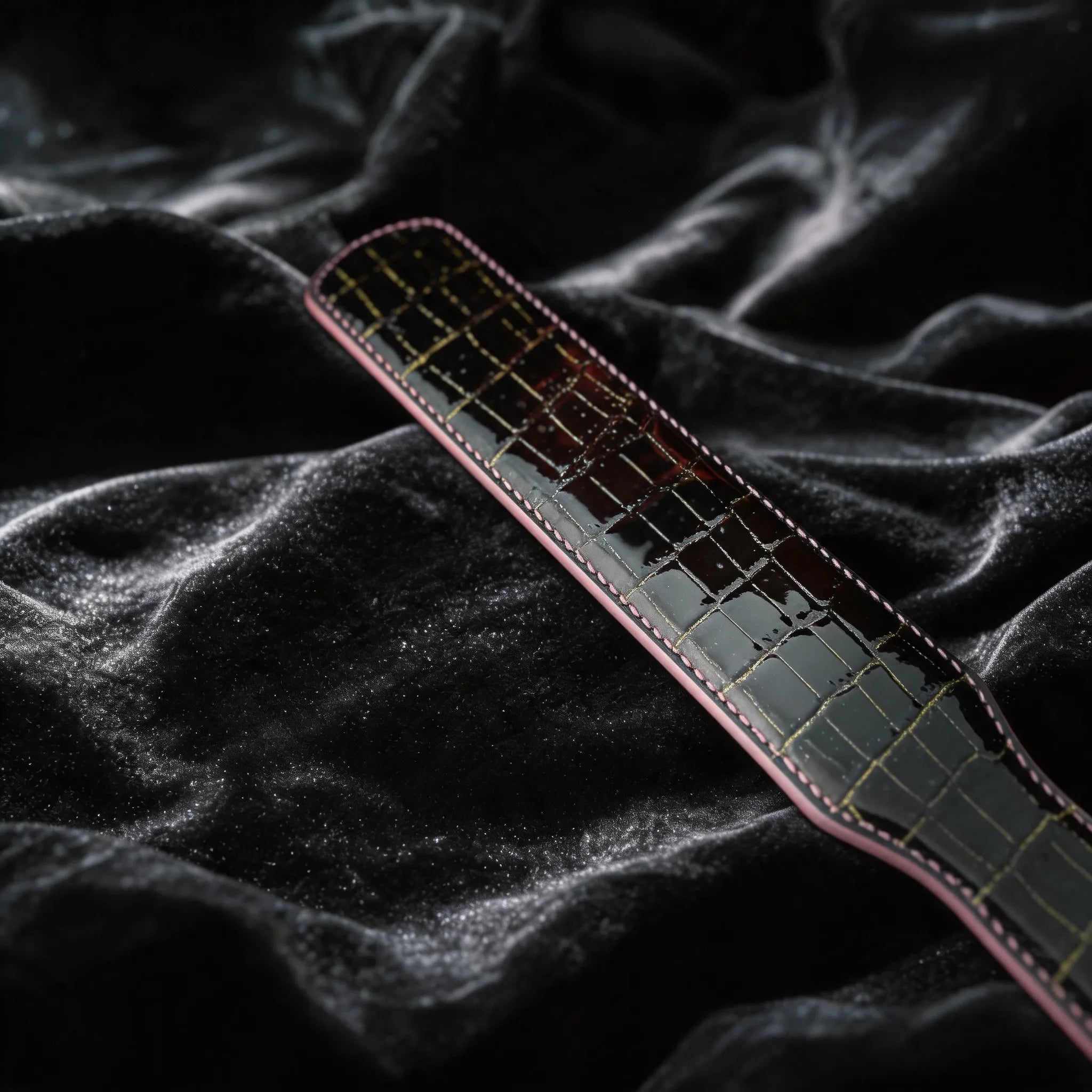 Noir Grid Patent Texture Leather Paddle hand-held studio detail showing grid texture and glossy edge.
