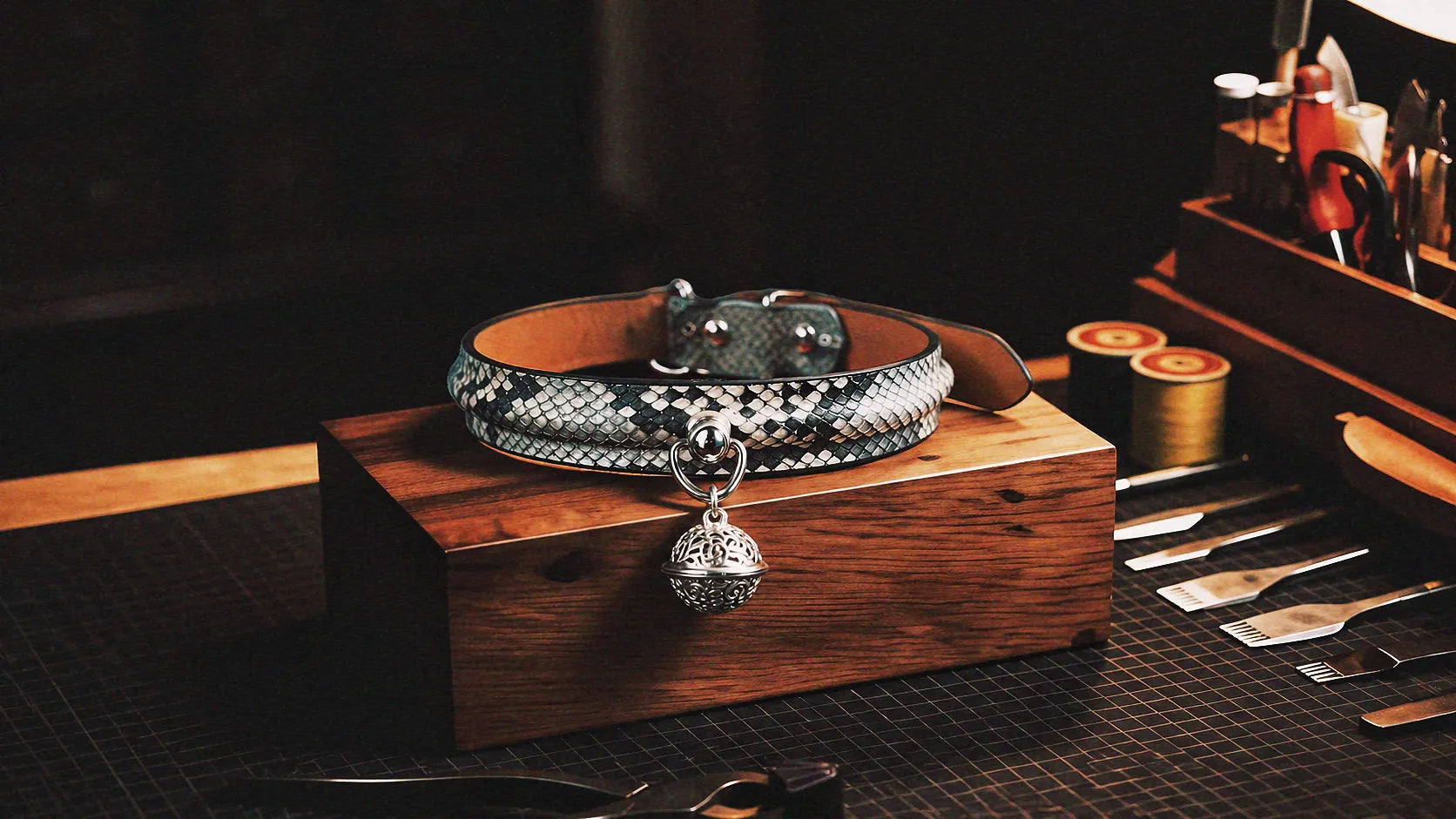 Python Echo Bell Leather Collar warm tabletop studio scene with wooden box, white and black python-textured leather, and bell charm.