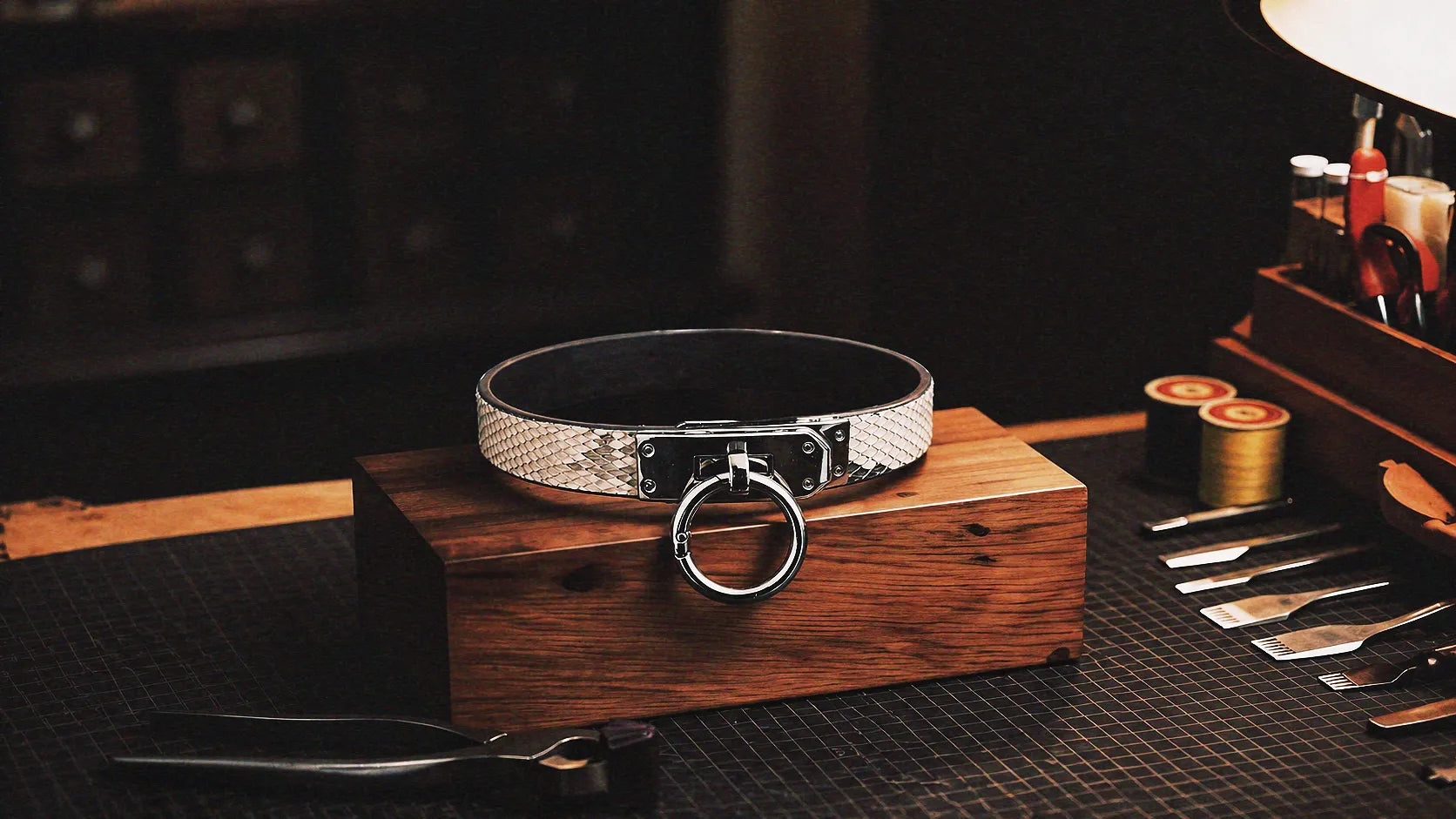 Python Lock O-Ring Leather Collar warm tabletop studio scene with wooden box, white and black python-textured leather, and O-ring front.