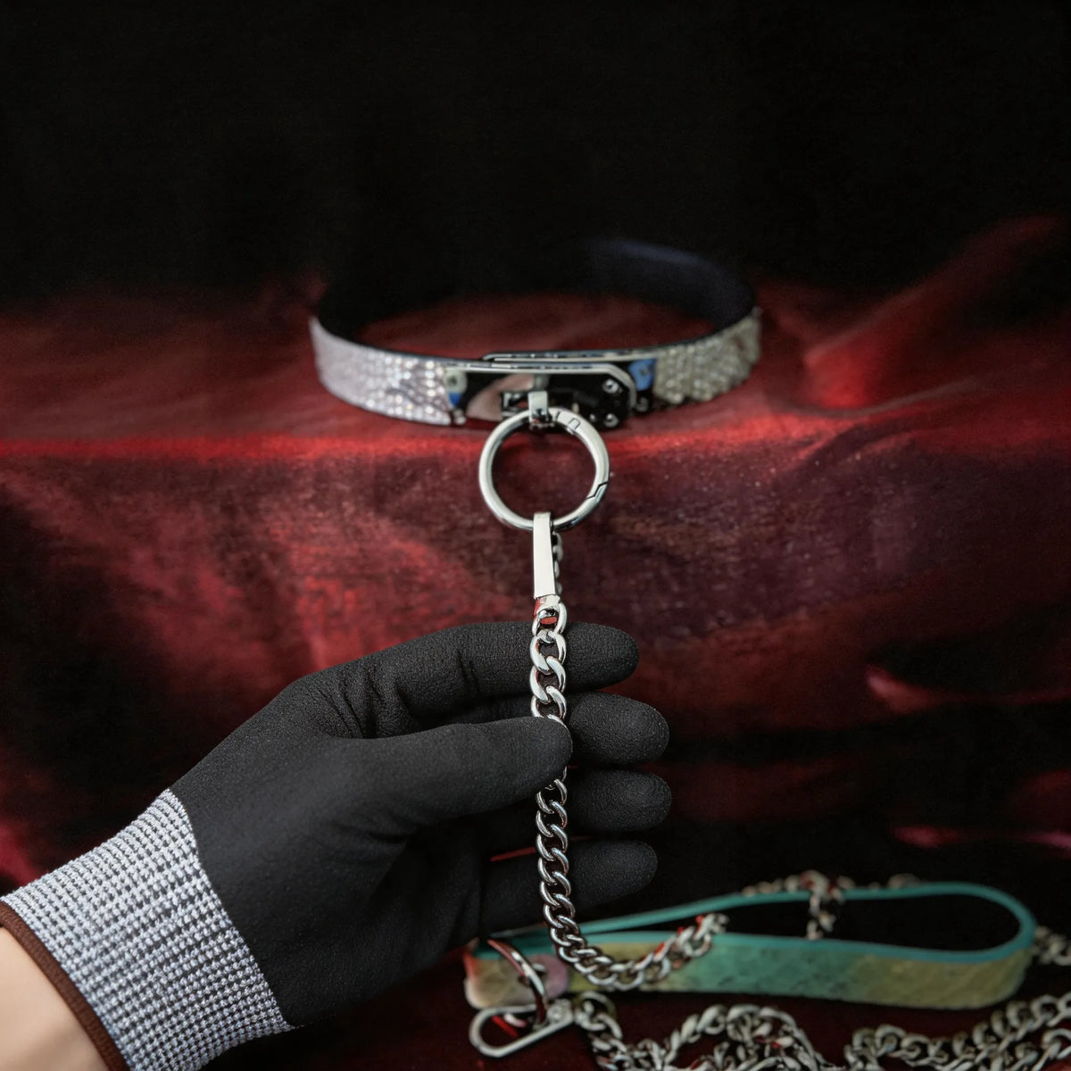 Python Lock O-Ring Leather Collar hand-held red satin scene with white and black leather and silver chain hardware.