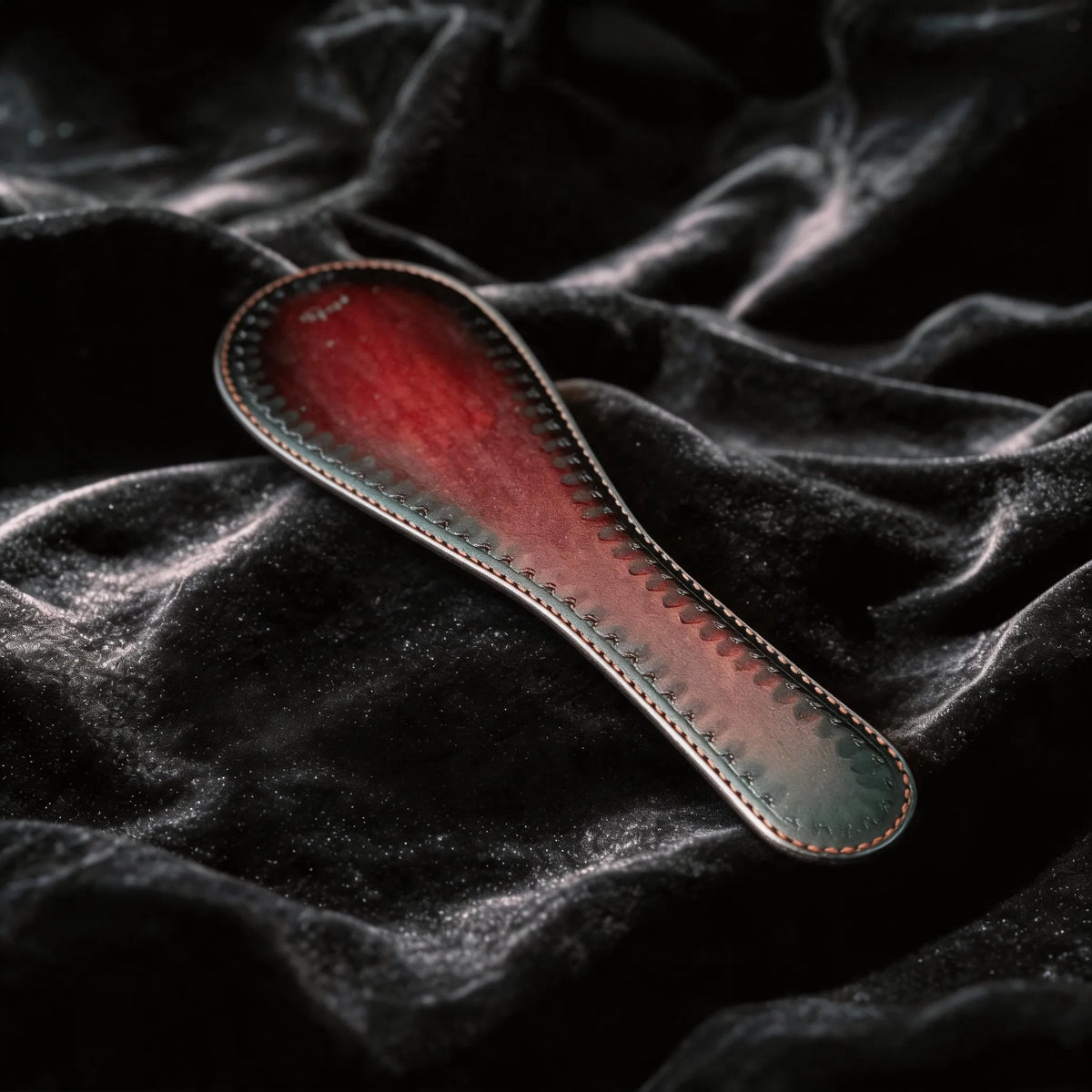 Scarlet Scale Textured Leather Paddle angled on black satin, showing crimson and black leather and scale texture.