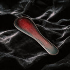 Scarlet Scale Textured Leather Paddle angled on black satin, showing crimson and black leather and scale texture.