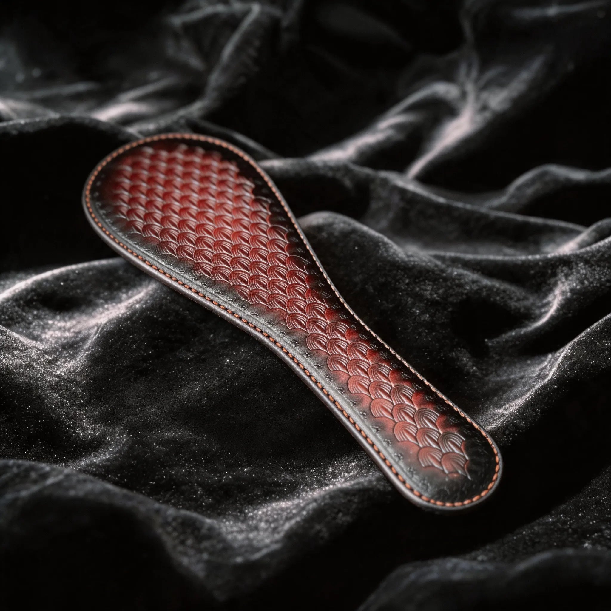 Scarlet Scale Textured Leather Paddle crimson and black leather paddle on black satin with scale texture.