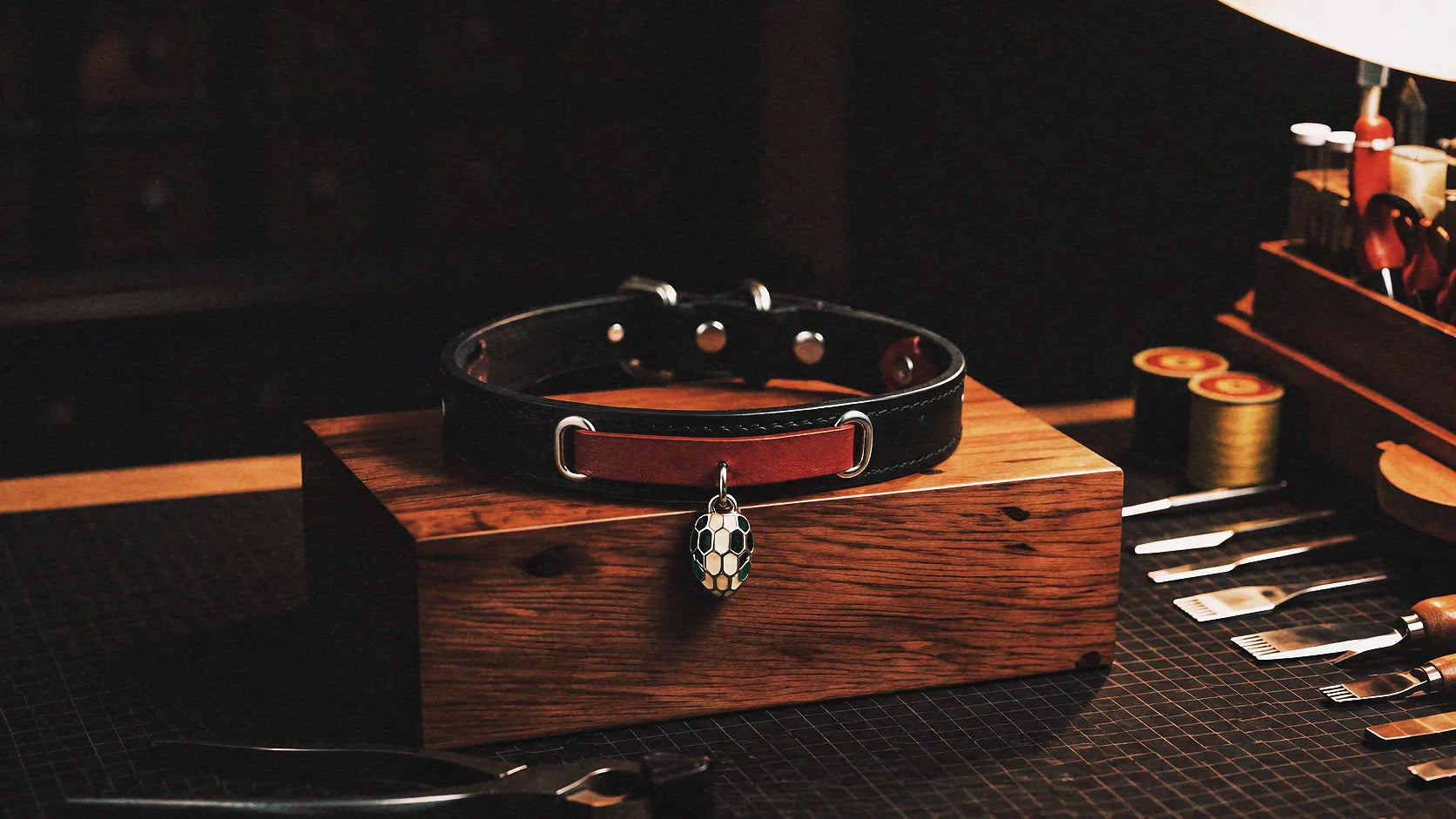 Serpent Mark Pendant Leather Collar warm tabletop studio scene with wooden box, black and crimson leather, and serpent pendant.
