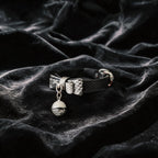 Serpentine Grace Bow Bell Leather Collar angled on black satin, showing black and white python-textured leather and bow and bell charm.