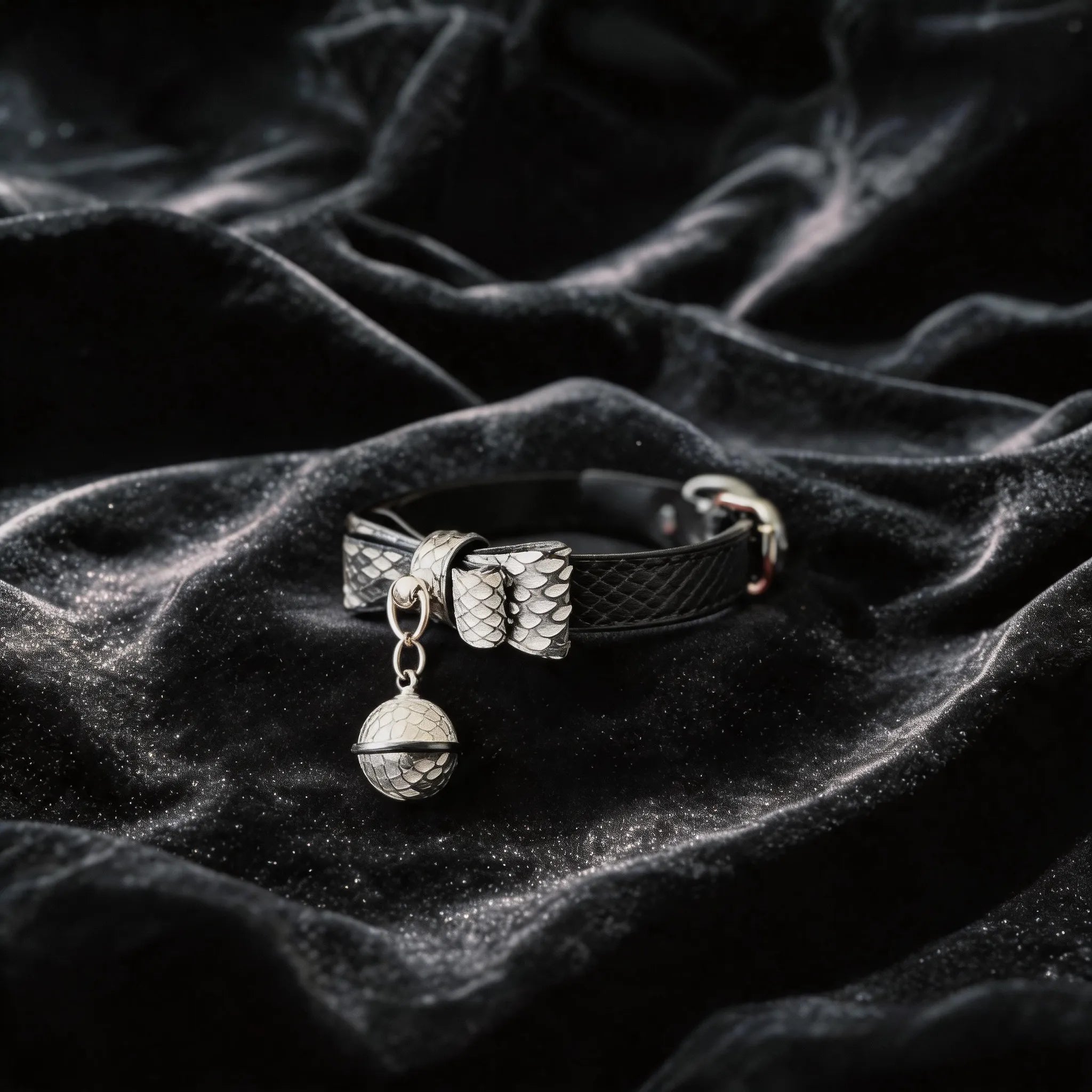 Serpentine Grace Bow Bell Leather Collar angled on black satin, showing black and white python-textured leather and bow and bell charm.