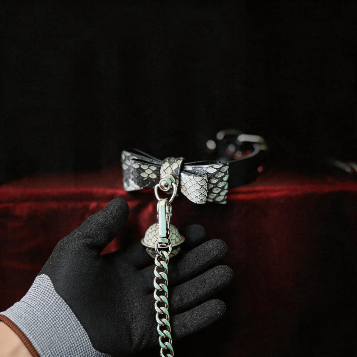Serpentine Grace Bow Bell Leather Collar hand-held studio detail showing bow and bell charm and silver chain hardware.