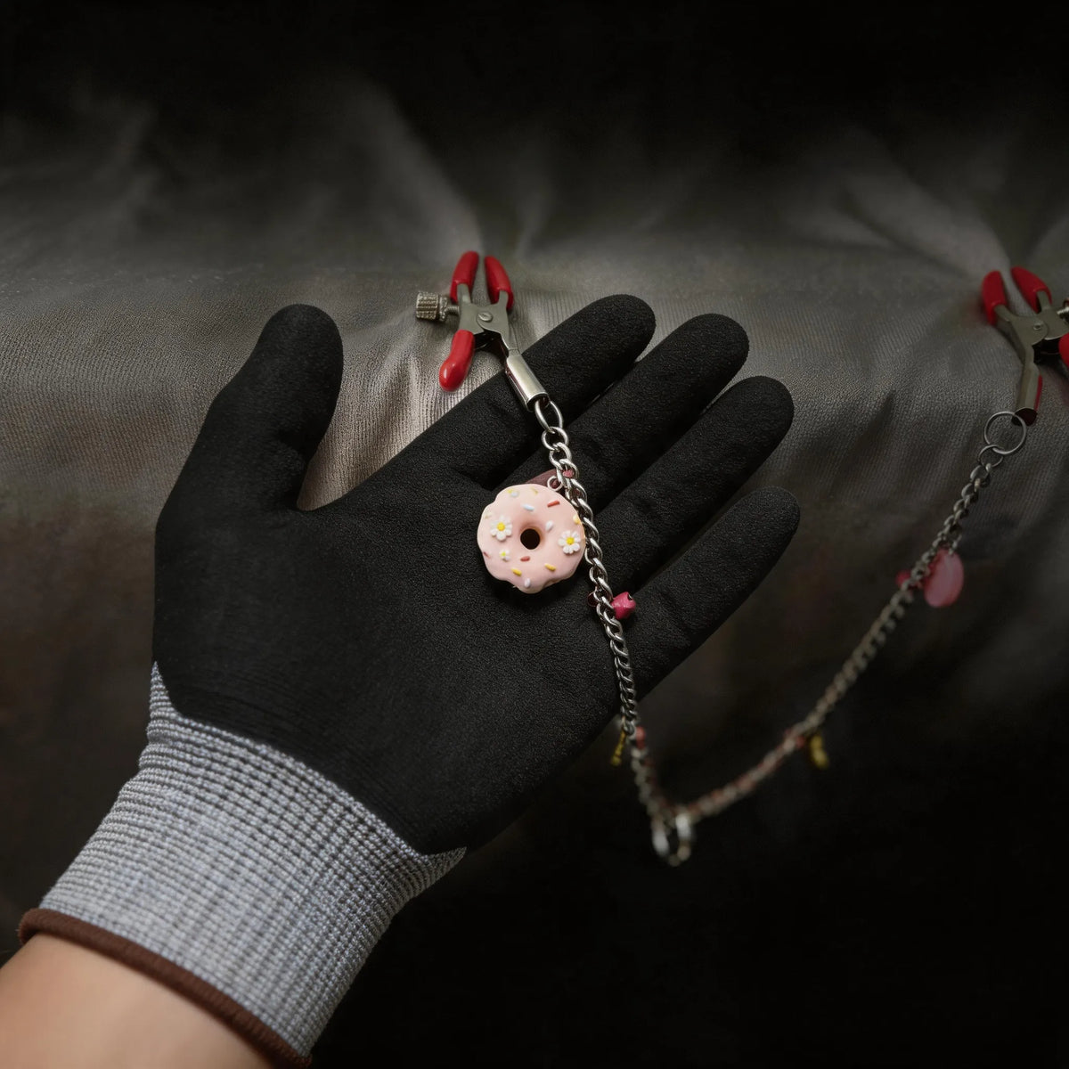 Sugar Tease Candy Charm Metal Nipple Clamps hand-held studio detail showing candy charm and chain hardware.