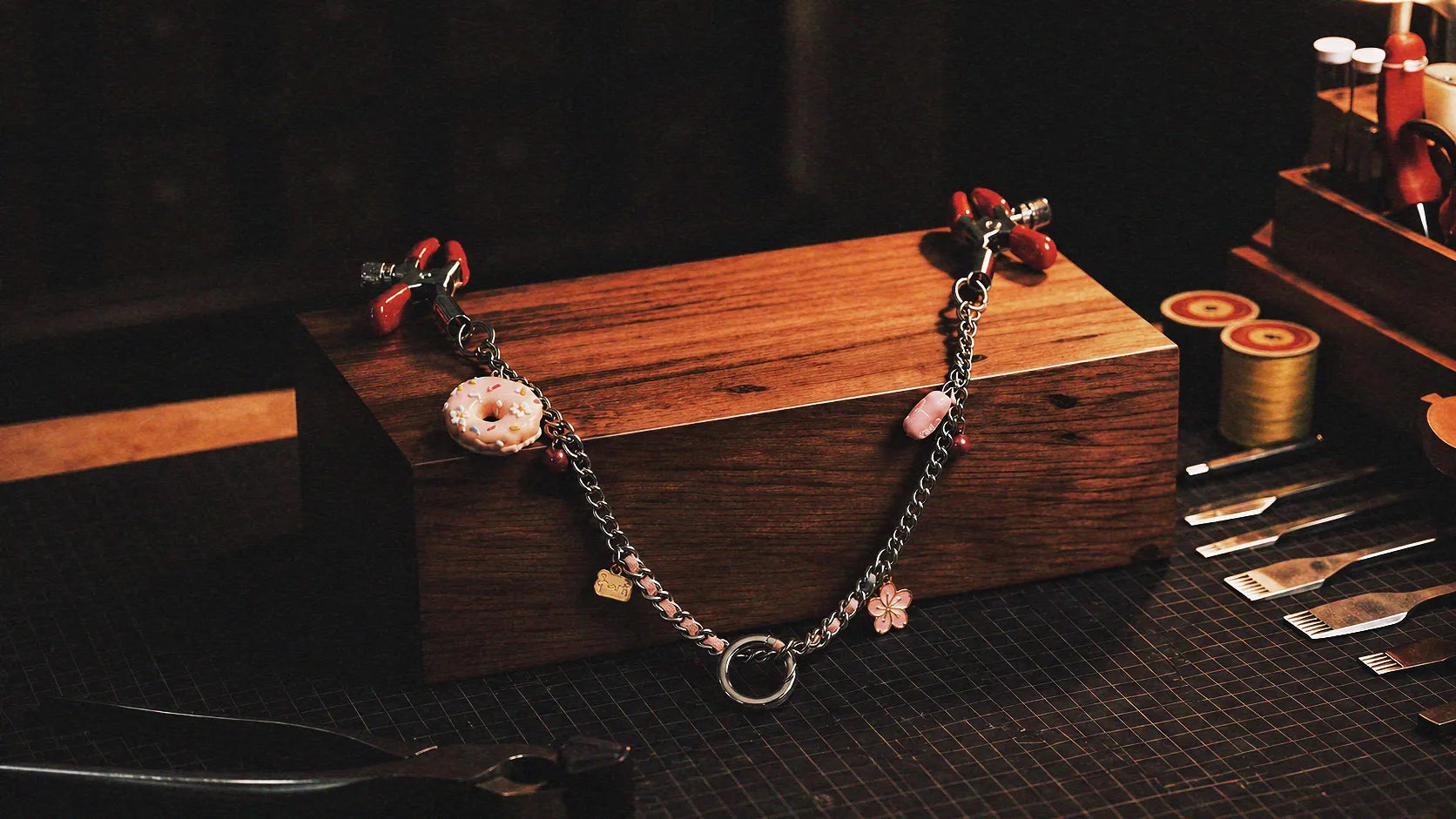 Sugar Tease Candy Charm Metal Nipple Clamps warm tabletop studio scene with wooden box, silver and red metal, and candy charm.